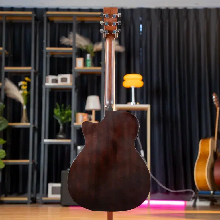 Back view of a dark wood acoustic guitar on a stand in a studio showroom with shelving and a bright orange chair in the background. ขายราคาพิเศษ