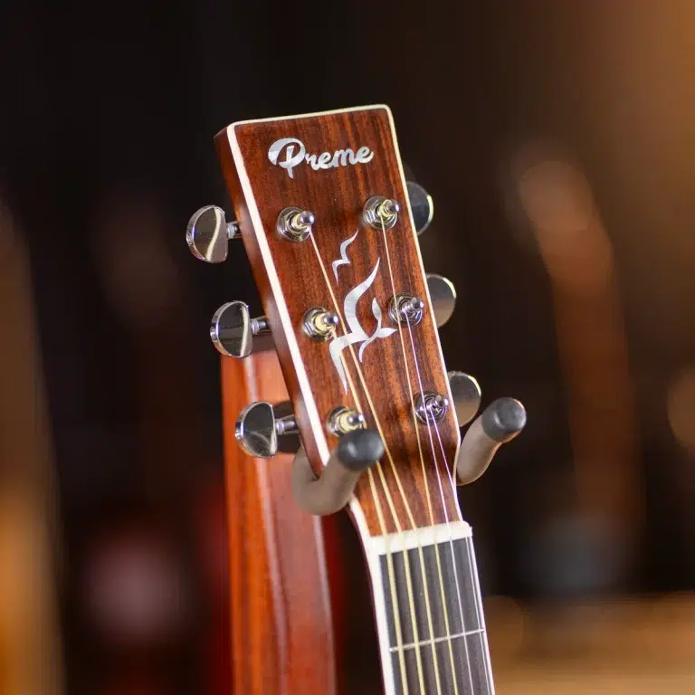 Close-up of a wooden guitar headstock with six metal tuning pegs, strings, and a 'Preme' logo visible on the headstock. ขายราคาพิเศษ