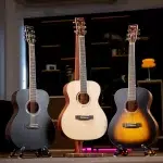 Three acoustic guitars on stands in a showroom, featuring dark, natural, and sunburst finishes from left to right. ลดราคาพิเศษ