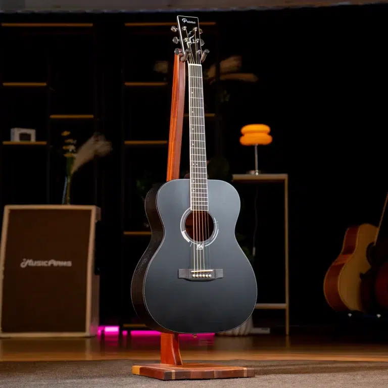 Black acoustic guitar on a wooden stand center-stage in a dim music shop or studio, with other gear blurred in the background. ขายราคาพิเศษ