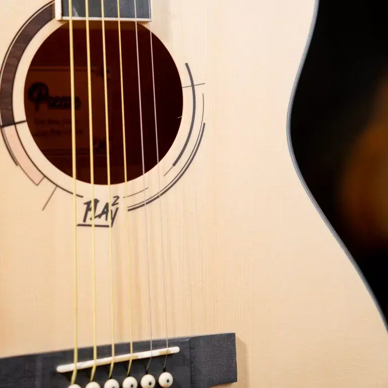 Close-up of a light-colored acoustic guitar showing the sound hole, decorative rosette, six strings, and the bridge with pins. ขายราคาพิเศษ