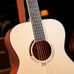 Close-up of an acoustic guitar with a light wood body, soundhole, and steel strings across the fretboard. ขายราคาพิเศษ