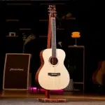 Acoustic guitar on a wooden stand center stage with warm lighting and stage gear in the background. ขายราคาพิเศษ