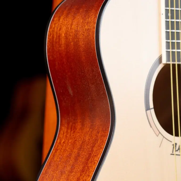Close-up of an acoustic guitar's body, highlighting the reddish wood grain and edge near the binding and soundhole on the right side. ขายราคาพิเศษ