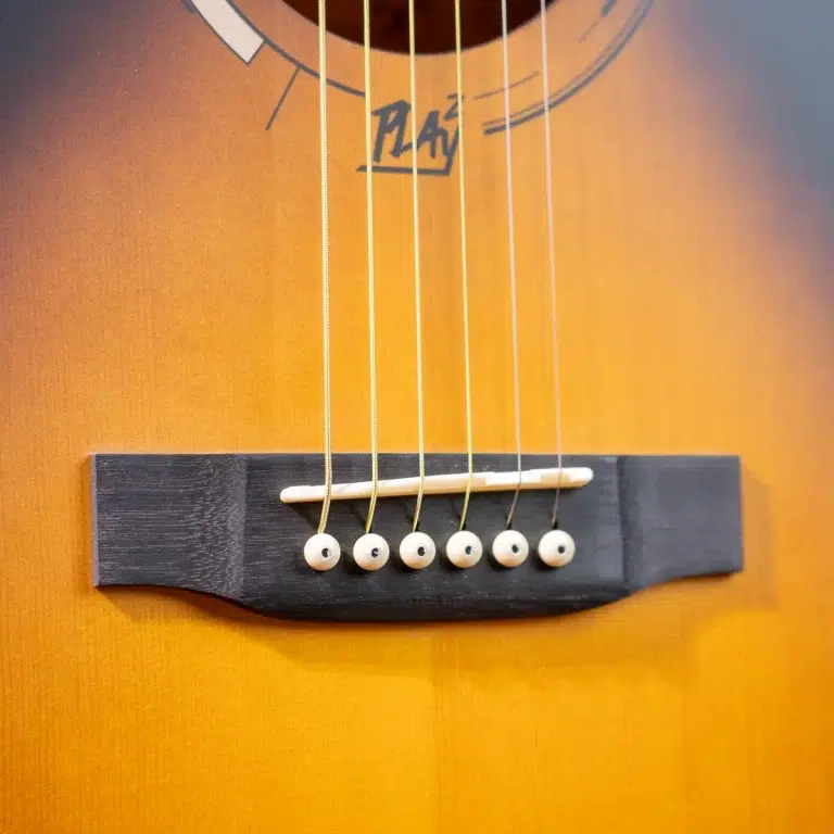Close-up of an acoustic guitar bridge with strings anchored by white bridge pins on a sunburst body, showing the saddle and strings. ขายราคาพิเศษ