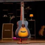 Sunburst acoustic guitar on a wooden stand center stage, with warm lighting and stage equipment in the background. ขายราคาพิเศษ