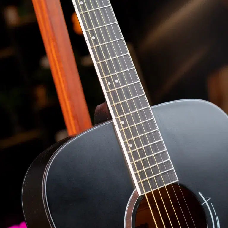Close-up of a dark gray acoustic guitar with the neck and strings in focus, resting against a wooden support. ขายราคาพิเศษ