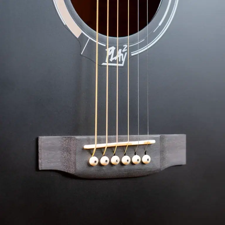 Close-up of a black acoustic guitar showing six strings anchored at the bridge over a dark saddle, with part of the soundhole visible. ขายราคาพิเศษ