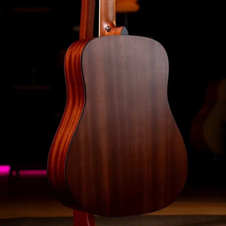 Back view of an acoustic guitar with a dark wood body and lighter sides, standing on a stand in a dimly lit studio. ขายราคาพิเศษ
