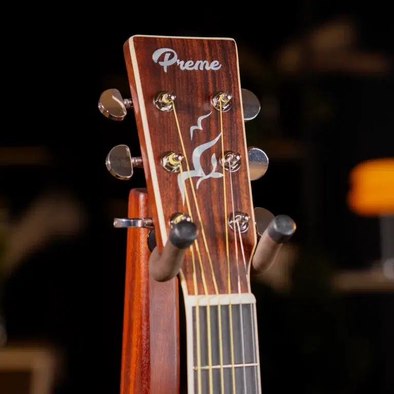 Close-up of a wooden guitar headstock on a stand, with chrome tuners, six strings, and the 'Preme' logo plus a white flame design. ขายราคาพิเศษ