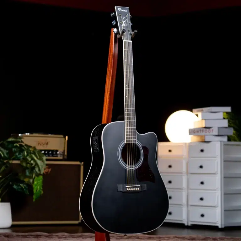Black acoustic guitar on a wooden stand in a home studio setup with an amp, plants, and white drawers in the background ขายราคาพิเศษ