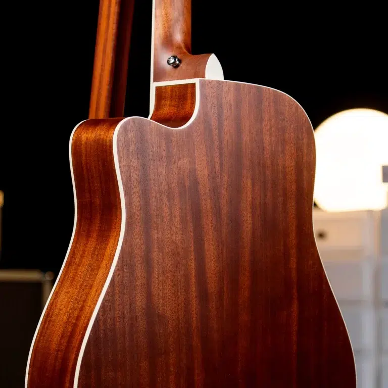 Close-up of the back and side of a mahogany acoustic guitar, showing the wood grain and white binding against a dark background. ขายราคาพิเศษ