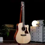 Light-colored acoustic guitar on a stand in a studio setup, with a speaker amp on the left and a round lamp on the right. ขายราคาพิเศษ