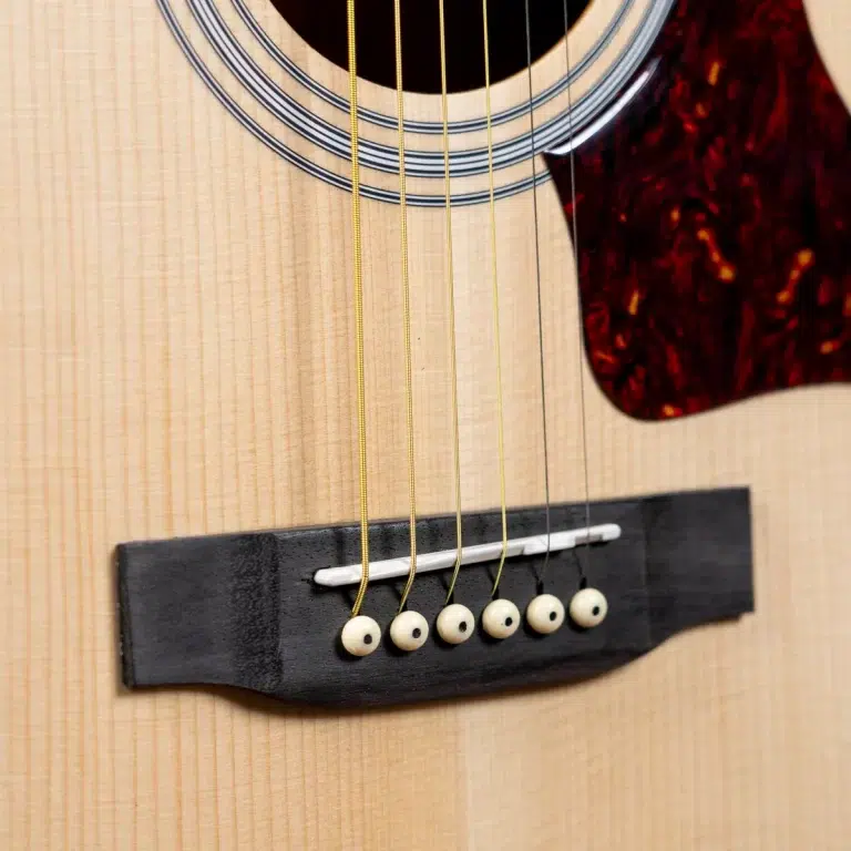 Close-up of an acoustic guitar's body showing the sound hole, strings, and bridge with white bridge pins. ขายราคาพิเศษ