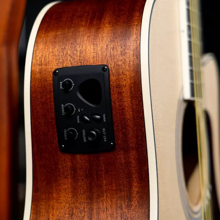Close-up of an acoustic guitar body showing a dark electronic control panel with knobs and a soundhole cutout on a warm brown wood finish ขายราคาพิเศษ