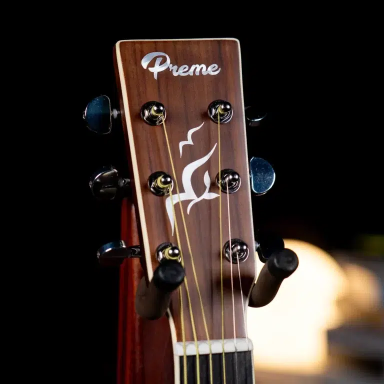 Close-up of a wooden guitar headstock with six tuning pegs, strings, and the brand name 'Preme' on dark background. ขายราคาพิเศษ