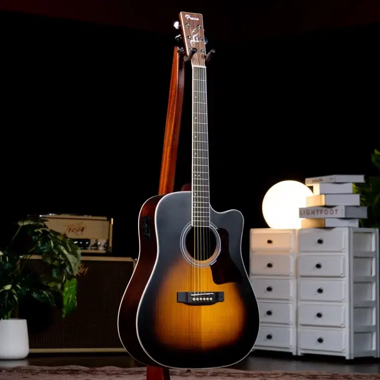 Sunburst acoustic guitar on a stand in a dim studio setting with warm lighting and gear in the background ขายราคาพิเศษ