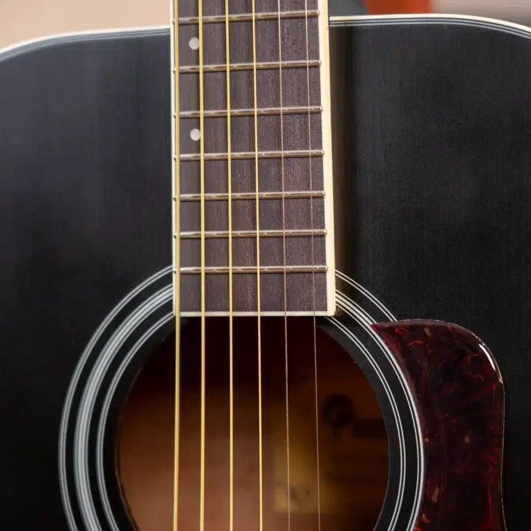 Close-up of a black acoustic guitar: fretboard with frets and six strings over the soundhole, with a tortoiseshell pickguard visible. ขายราคาพิเศษ