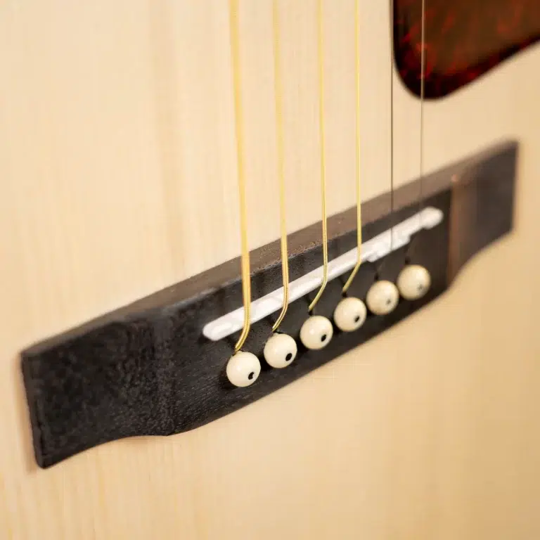Close-up of an acoustic guitar bridge with white bridge pins and light-colored strings anchored to a dark saddle plate ขายราคาพิเศษ