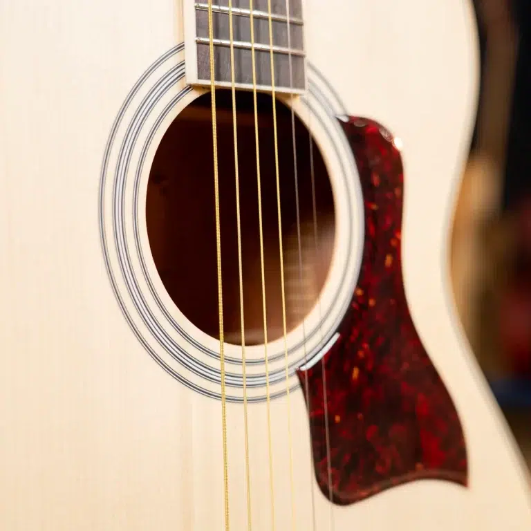 Close-up of an acoustic guitar: soundhole, six strings, and a tortoiseshell pickguard on a light wooden body ขายราคาพิเศษ