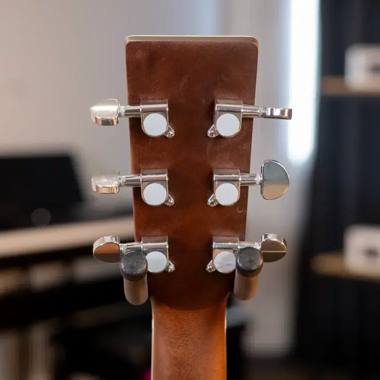 Back of a guitar headstock with six chrome tuners and brown wood, tuned pegs visible in a studio setting ขายราคาพิเศษ