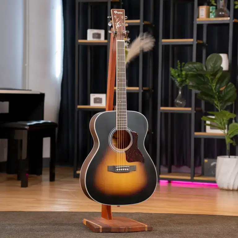 Sunburst acoustic guitar on a wooden display stand in a music store, with shelves, a piano, and plants in the background. ขายราคาพิเศษ