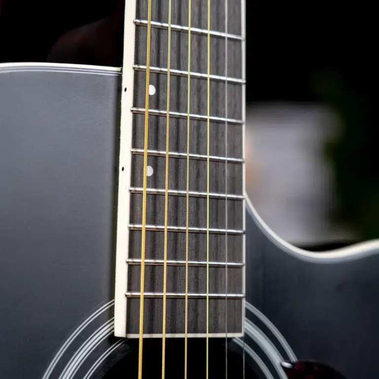 Close-up of a guitar neck with frets, strings, and fret markers on a dark body surface. ขายราคาพิเศษ
