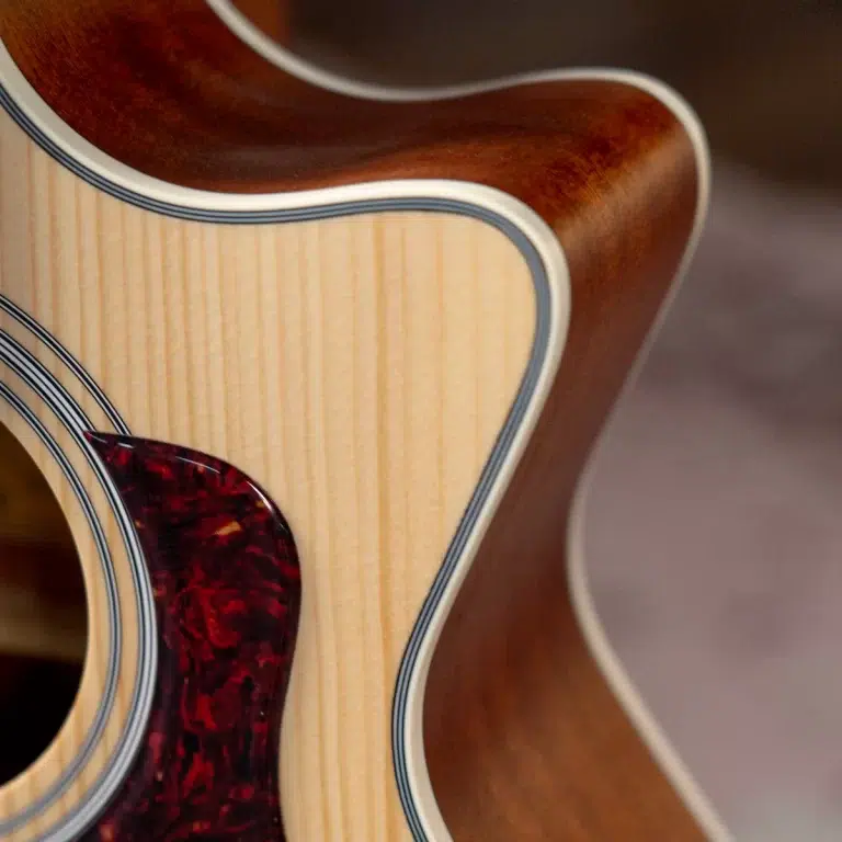 Close-up of an acoustic guitar body showing natural wood grain, cream binding, and a red tortoiseshell pickguard edge. ขายราคาพิเศษ