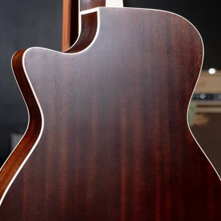 Close-up of the dark wood back of an acoustic guitar with white binding along the edges (mahogany grain visible). ขายราคาพิเศษ