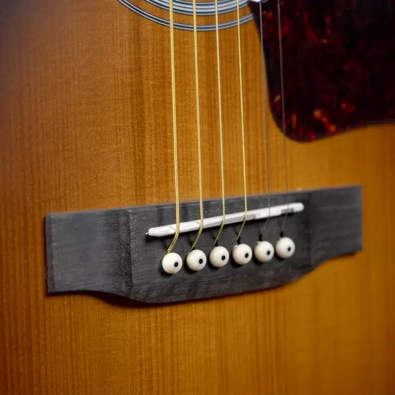 Close-up of an acoustic guitar bridge with white plastic pegs and saddled saddle on a wooden body, showing multiple strings attached ขายราคาพิเศษ
