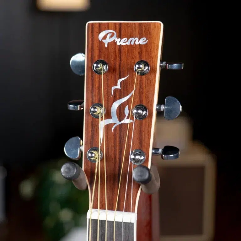 Close-up of a wooden guitar headstock with six tuning pegs and strings, featuring the 'Preme' logo on the wood surface. ขายราคาพิเศษ