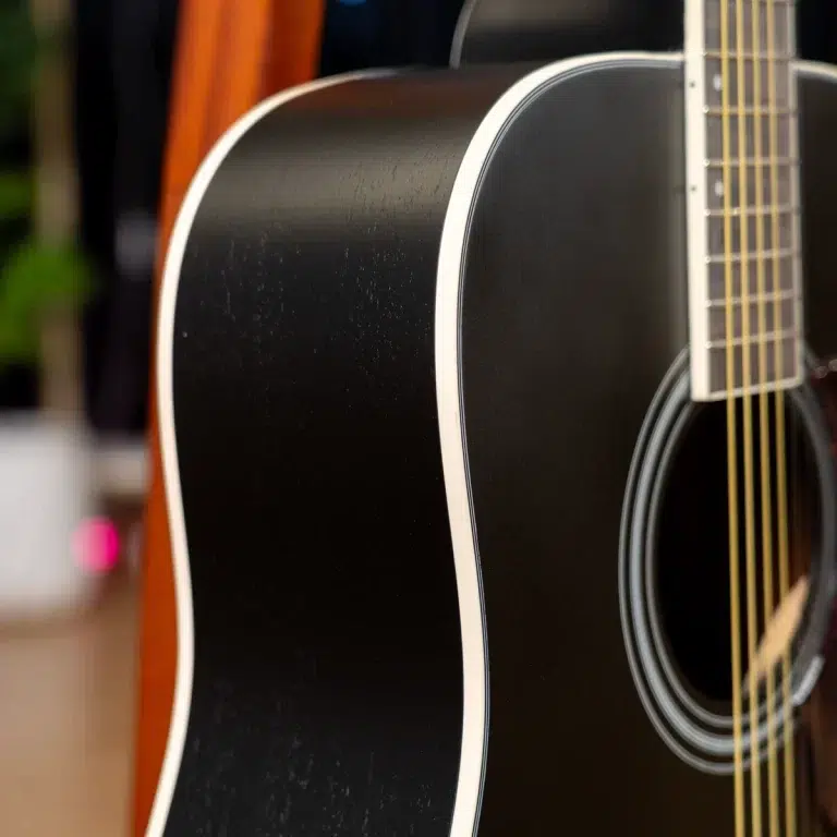Close-up of a black acoustic guitar body with white binding and golden strings along the edge of the fretboard. ขายราคาพิเศษ