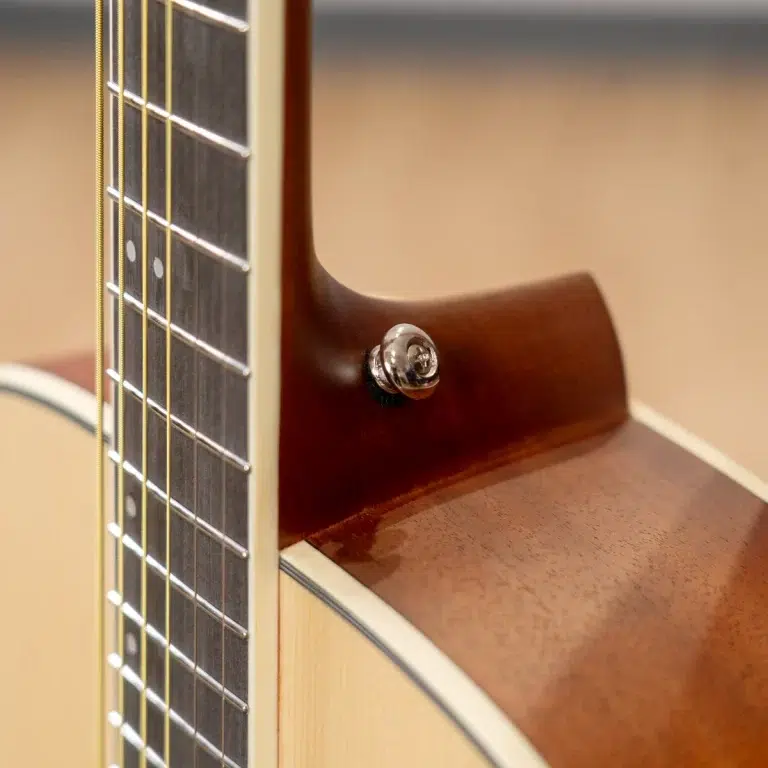 Close-up of an acoustic guitar neck and body, showing frets, strings, and a chrome strap pin near the heel. ขายราคาพิเศษ