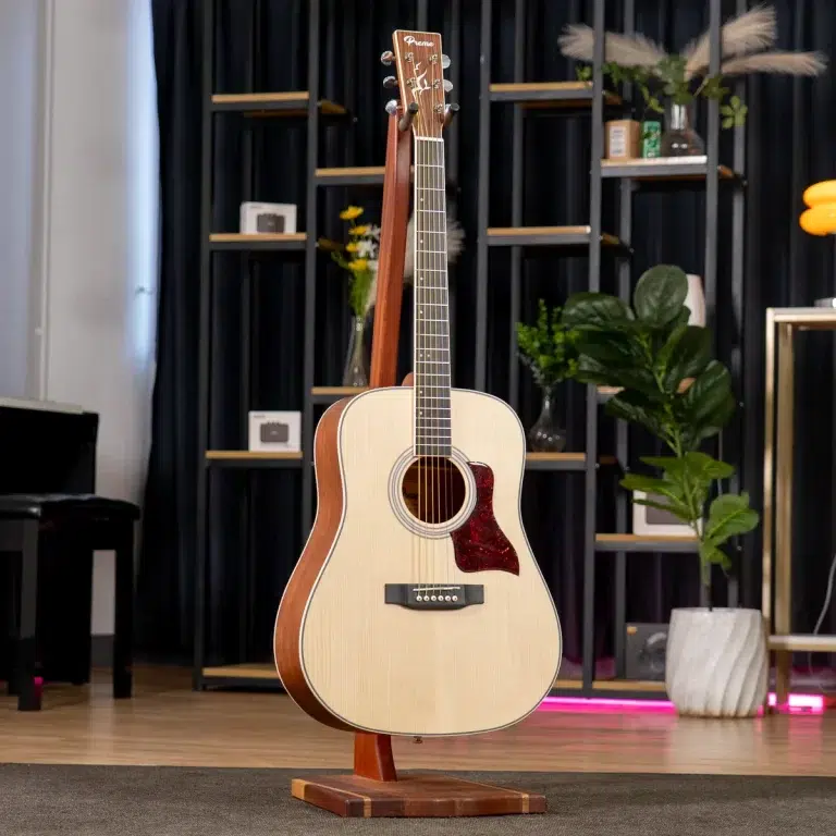 Acoustic guitar on a wooden stand in a modern showroom with shelves, plants, and warm lighting behind it. ขายราคาพิเศษ