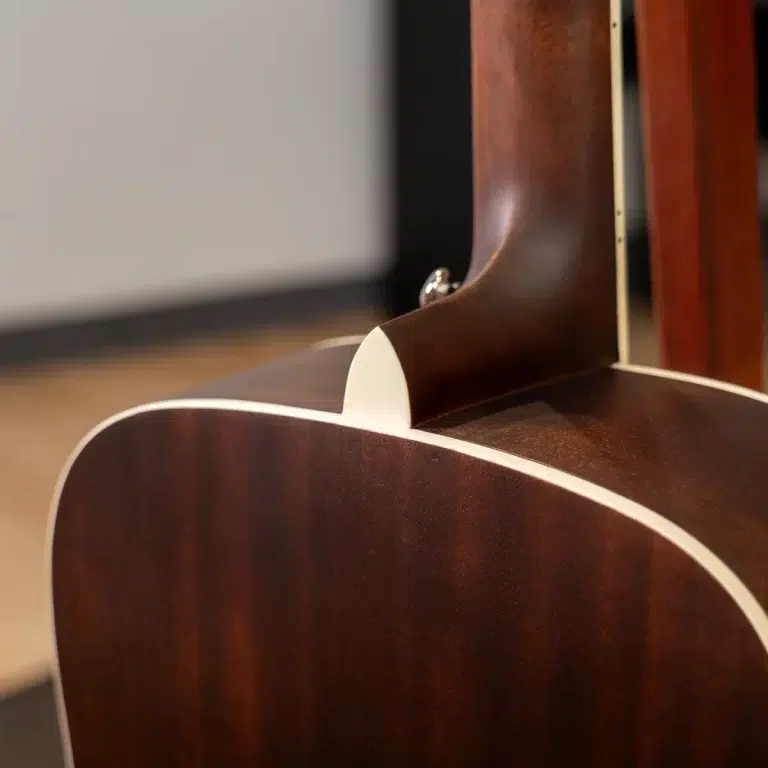 Close-up of a glossy brown acoustic guitar showing the neck heel, body binding, and wood grain detail. ขายราคาพิเศษ