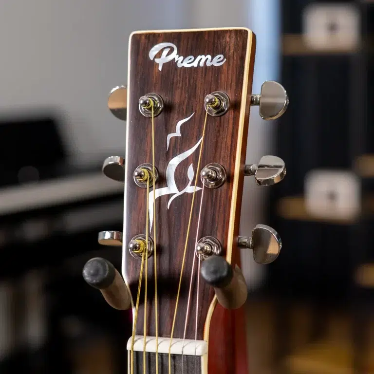 Close-up of a wooden guitar headstock with tuning pegs and a white flame inlay, and the 'Preme' logo visible on the top edge. ขายราคาพิเศษ