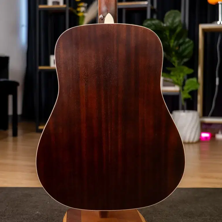Back of a dark brown acoustic guitar on a stand in a cozy indoor studio room with plants in the background. ขายราคาพิเศษ