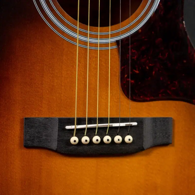Close-up of an acoustic guitar bridge with six strings and white bridge pins on a sunburst body. ขายราคาพิเศษ