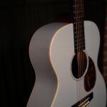 Close-up of a white acoustic guitar against a dark background, focusing on the curved body and strings. ขายราคาพิเศษ