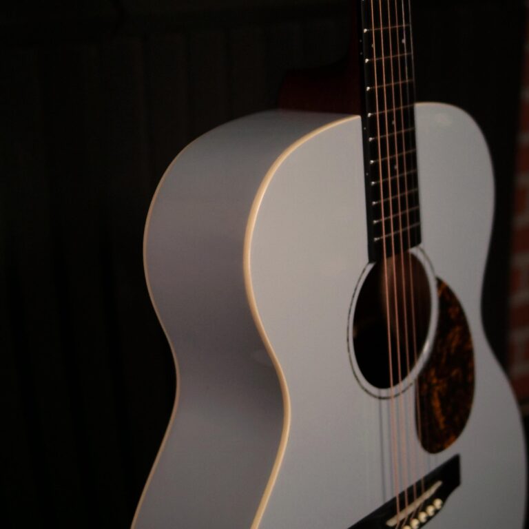 Close-up of a white acoustic guitar against a dark background, focusing on the curved body and strings. ขายราคาพิเศษ