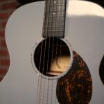 Light gray acoustic guitar close-up showing soundhole, six strings, and a tortoiseshell pickguard in the foreground. Note: concise and informative for screen readers, focusing on the image's meaning. ขายราคาพิเศษ