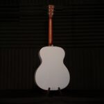 Back view of a white acoustic guitar on a stand in a dark recording studio. ขายราคาพิเศษ