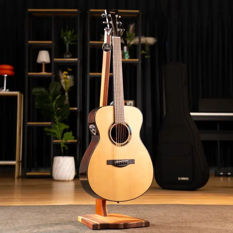 Acoustic guitar on a wooden stand in a showroom with shelves and plants in the background ขายราคาพิเศษ