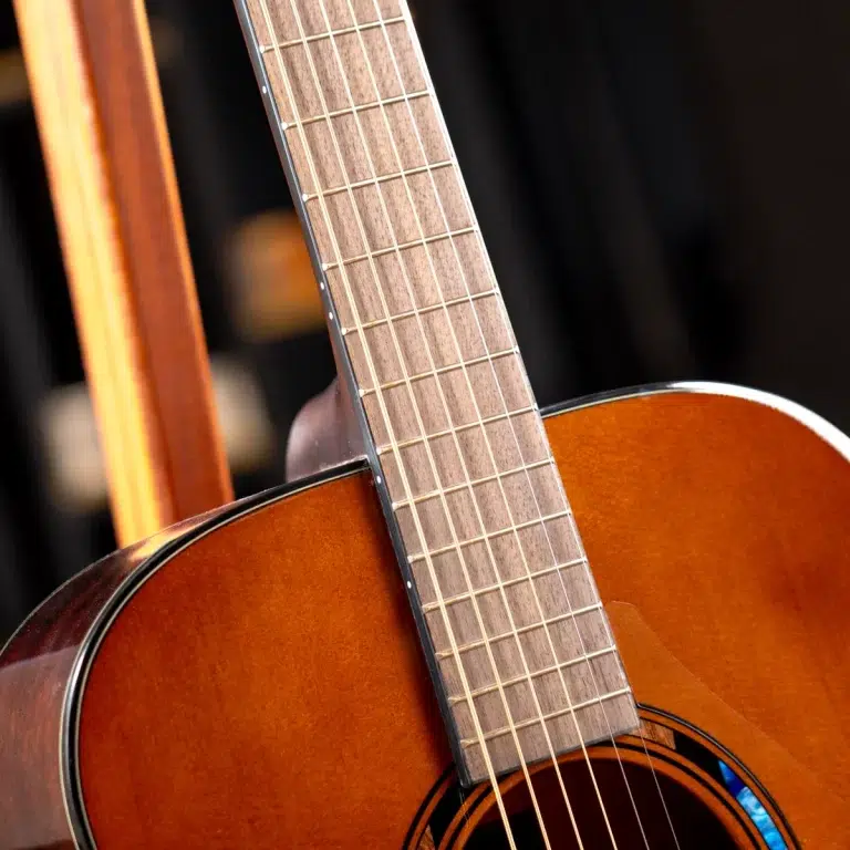 Close-up of a wooden acoustic guitar neck with frets and strings over the body edge visible in warm lighting ขายราคาพิเศษ