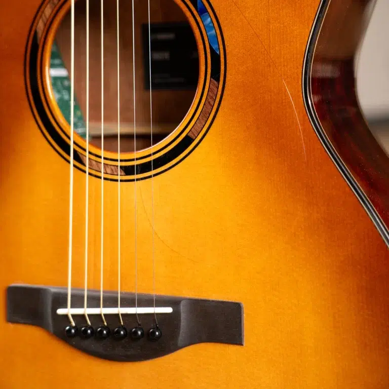 Close-up of an acoustic guitar body showing strings over the bridge and soundhole in warm amber finish. ขายราคาพิเศษ
