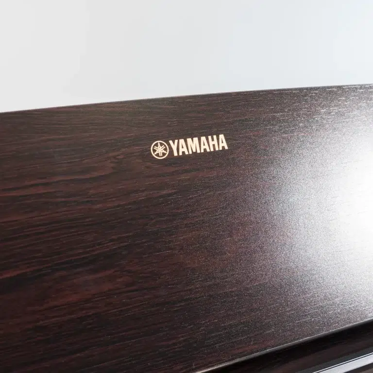 Close-up of a dark wood piano panel featuring a gold Yamaha logo and emblem ขายราคาพิเศษ