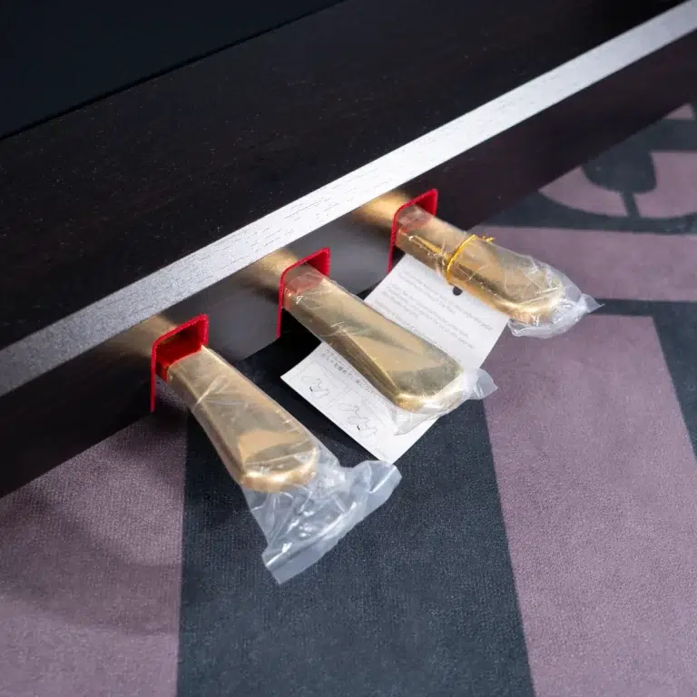 Close-up of three gold-colored metal levers attached to a dark edge, each wrapped in plastic with red mounting brackets and a small instruction sheet nearby. ขายราคาพิเศษ