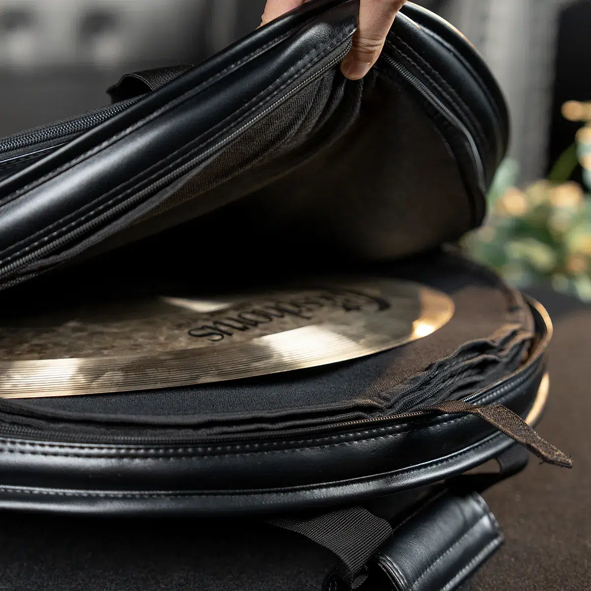 Close-up of a hand opening a black bag to reveal a shiny circular cymbal or metal disc inside