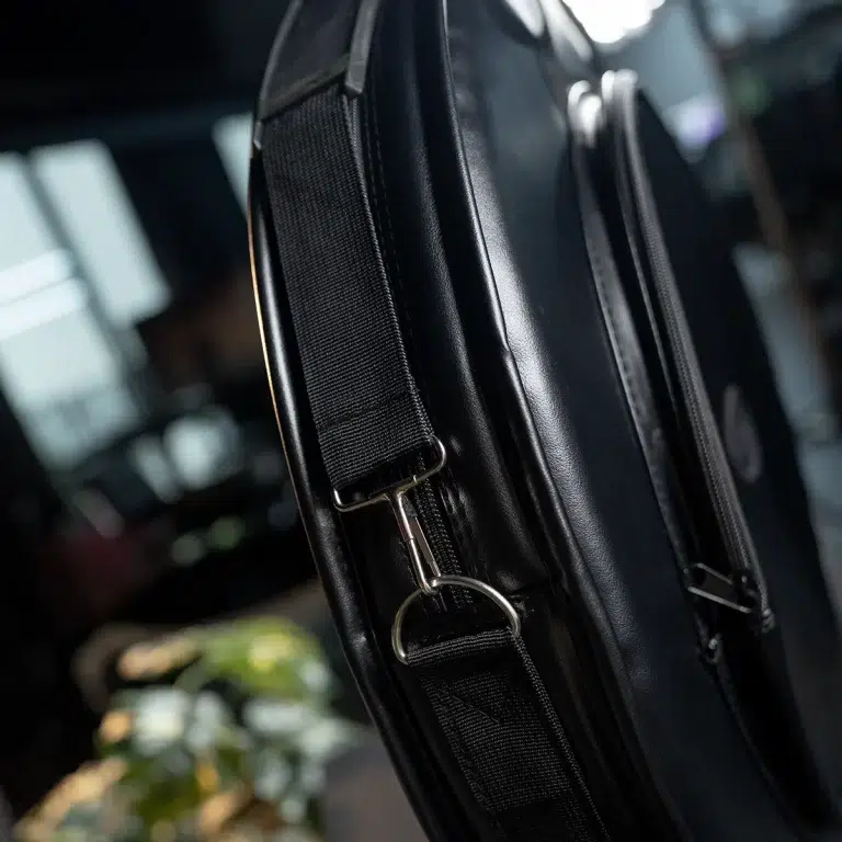Close-up of a black leather bag showing the adjustable strap with a metal buckle and a zipper pull on the side. ขายราคาพิเศษ