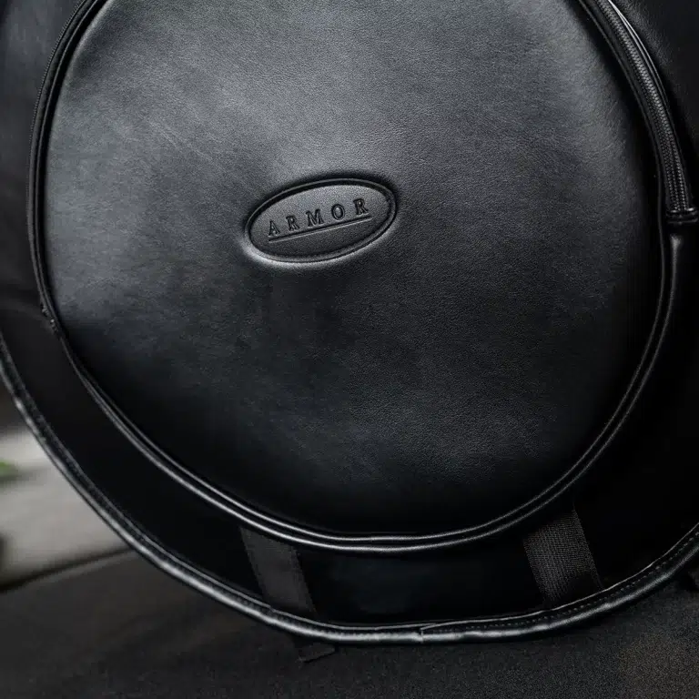Close-up of a black circular leather bag with an oval patch embossed with the word ARMOR ขายราคาพิเศษ